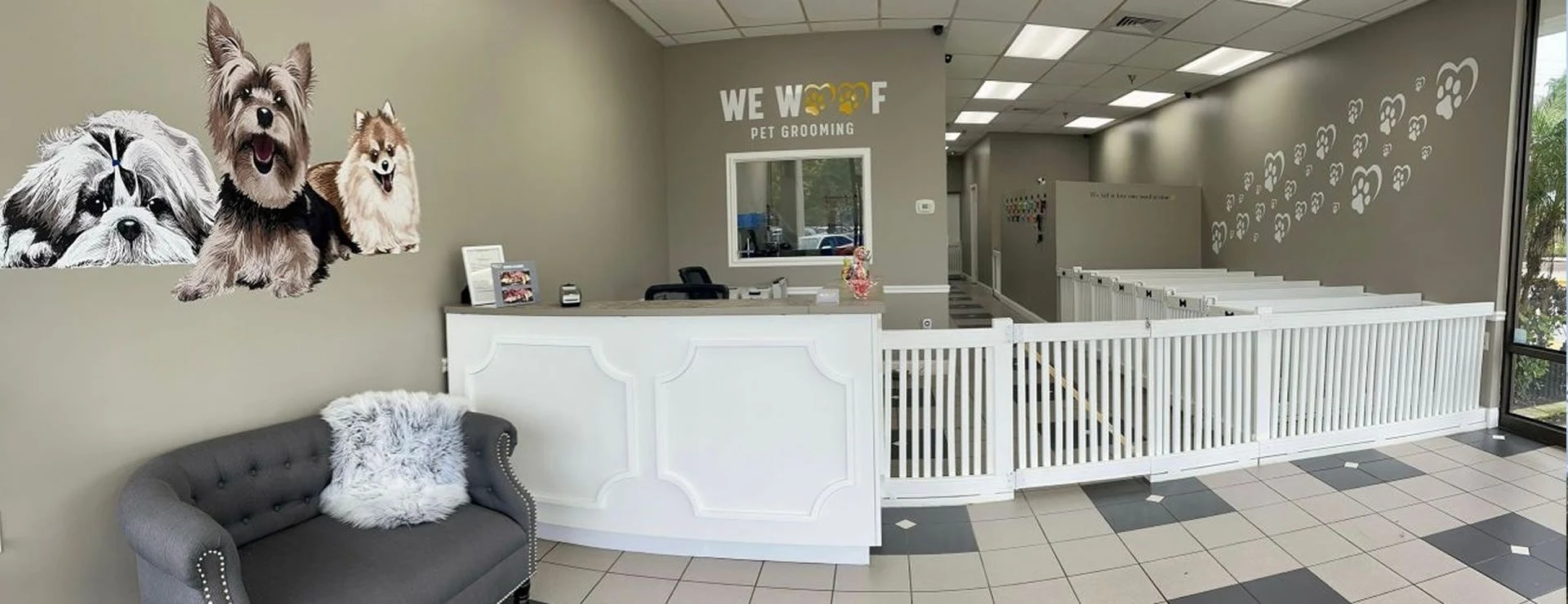 The We Woof salon with a gray pet sofa, dog mural, reception desk and white grooming-area gates